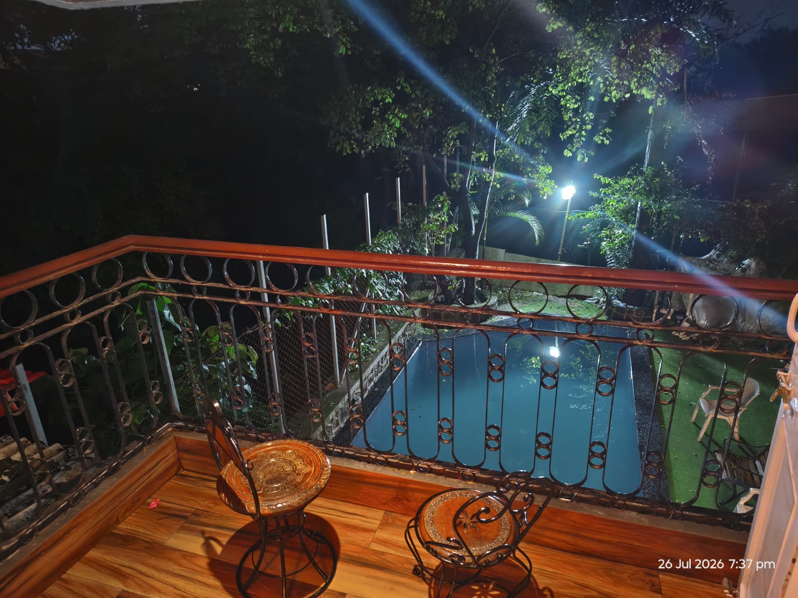 Balcony with wooden flooring overlooking the illuminated private pool at the Lonavala villa
